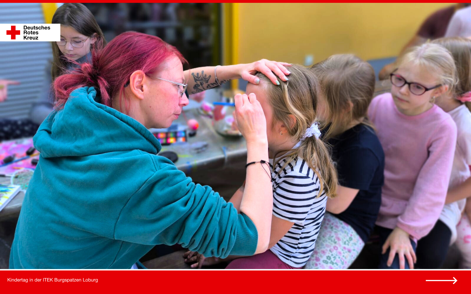 Mitarbeiterin schminkt ein Kind beim Kinderschminken während des DRK-Kindertags in der Kita Burgspatzen Loburg; weitere Kinder warten in der Reihe.