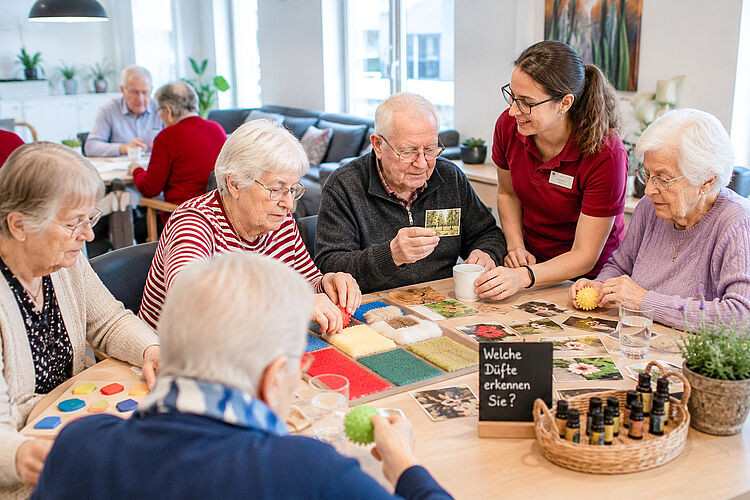 Seniorinnen und Senioren nehmen gemeinsam mit einer Mitarbeiterin an einem Wahrnehmungs- und Orientierungstraining in der Tagespflege teil.