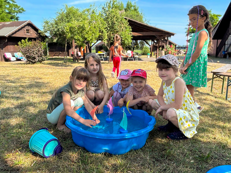 Kinder der DRK-Kita „Rasselbande“ hocken lachend um eine blaue Wasserschale und spielen mit kleinen selbstgebastelten Segelbooten auf dem Bauernhof in Königsrode.