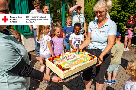 Kinder und Erzieherinnen halten eine große Jubiläumstorte mit der Aufschrift „45 Jahre Kita“.