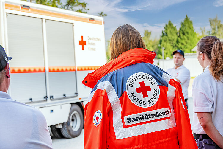 DRK-Sanitäterin in Einsatzjacke beim Dienstabend, während der Gruppenführer der Sanitätsgruppe den Ablauf zum Thema GW-San erklärt.