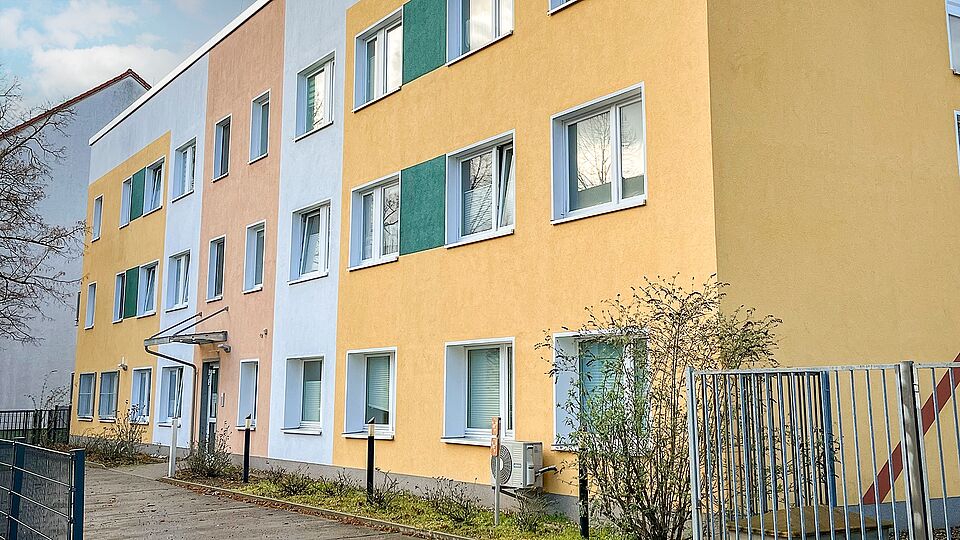 Fassade der DRK-Tagespflege Gommern mit gelben und grünen Farbflächen, barrierefreiem Eingang und mehreren Fenstern.