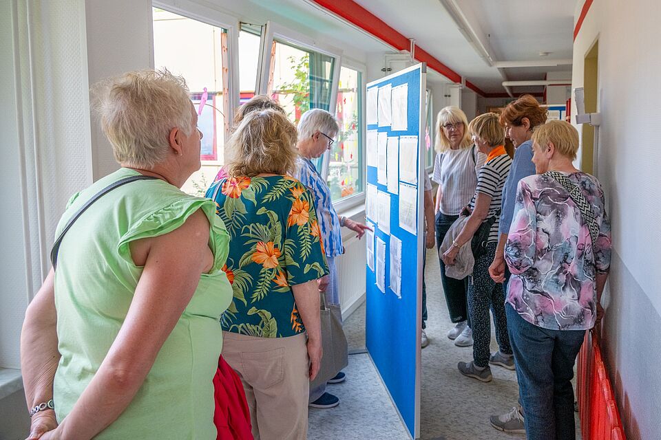 Eine Gruppe ehemaliger Erzieherinnen schaut sich im Kita-Flur alte Bilder und Dokumente an.
