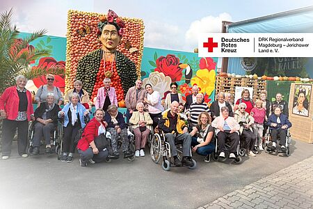 Gruppenfoto mit Seniorinnen, Senioren und Pflegekräften der DRK-Tagespflege Möckern vor einer bunten Wand mit Kürbisbild auf dem Spargelhof Klaistow.