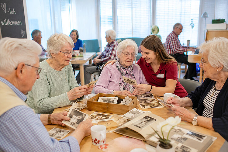 Seniorinnen und Senioren betrachten gemeinsam mit einer Mitarbeiterin alte Fotografien und Fotoalben im Rahmen der Erinnerungs- und Biografiearbeit.