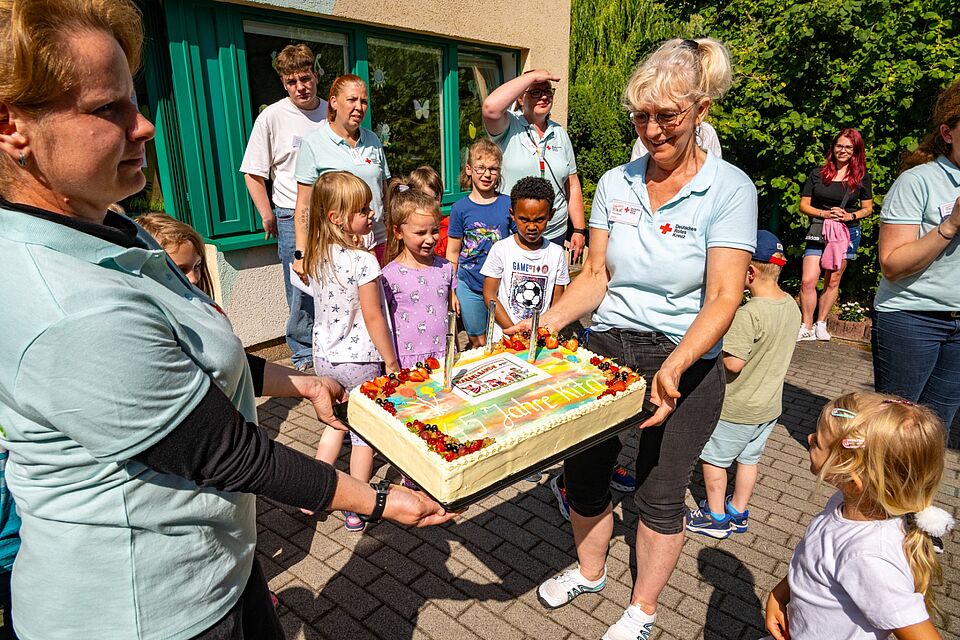 Kinder und Erzieherinnen halten eine große Jubiläumstorte mit der Aufschrift „45 Jahre Kita“.