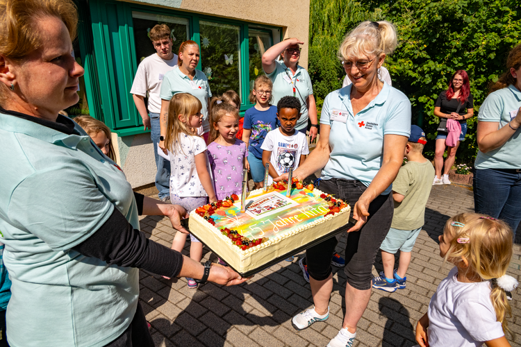 Kinder und Erzieherinnen halten eine große Jubiläumstorte mit der Aufschrift „45 Jahre Kita“.