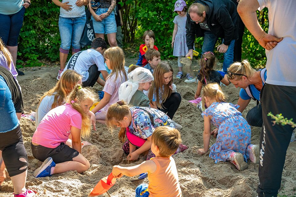 Viele Kinder graben gemeinsam im Sandkasten nach Schätzen.