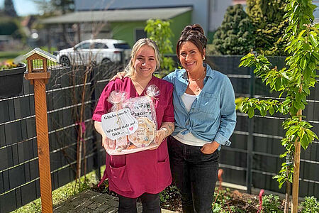 Zwei Frauen stehen im Außenbereich der DRK-Tagespflege Loburg; eine überreicht ein Geschenk zur bestandenen PAL-Weiterbildung