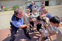 Kinder des DRK-Hortes „Ludwig Uhland“ probieren gemeinsam mit einem Polizeibeamten ein Einsatzschild aus.