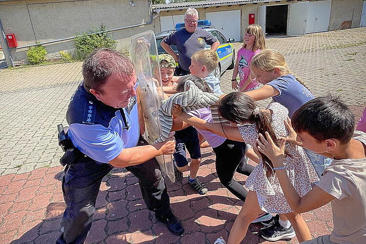 Hortkinder des DRK-Hortes „Ludwig Uhland“ zu Gast bei der Polizei Kinder des DRK-Hortes „Ludwig Uhland“ probieren gemeinsam mit einem Polizeibeamten ein Einsatzschild aus.
