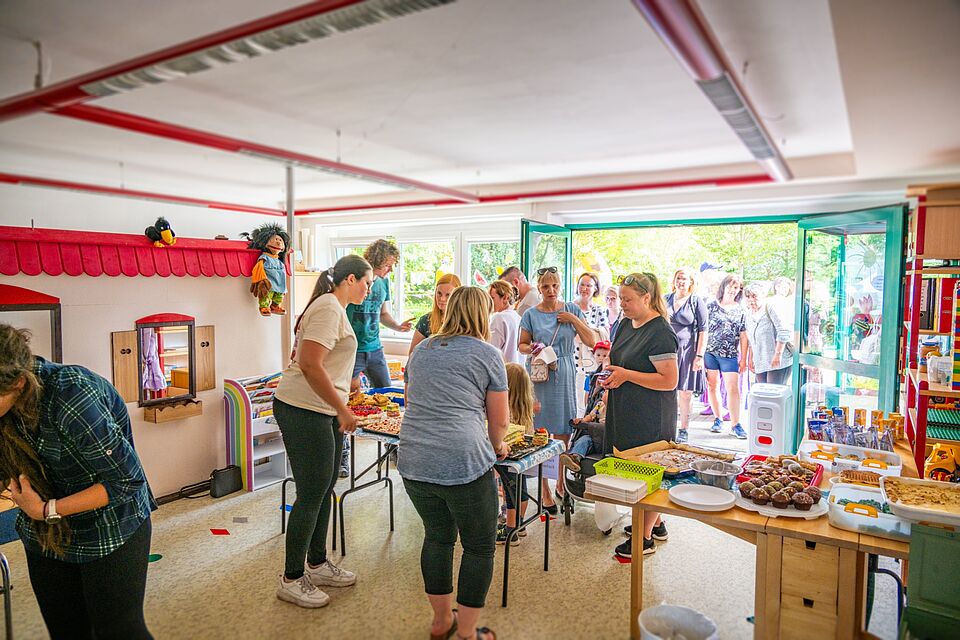 Menschen stehen in einem Gruppenraum am Buffet mit Kuchen und Muffins.