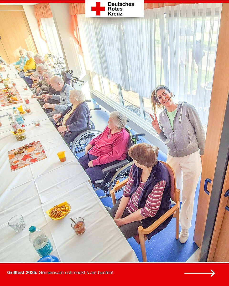 Bewohnerinnen und Bewohner sitzen am gedeckten Tisch beim Grillfest 2025, eine Mitarbeiterin lächelt in die Kamera.