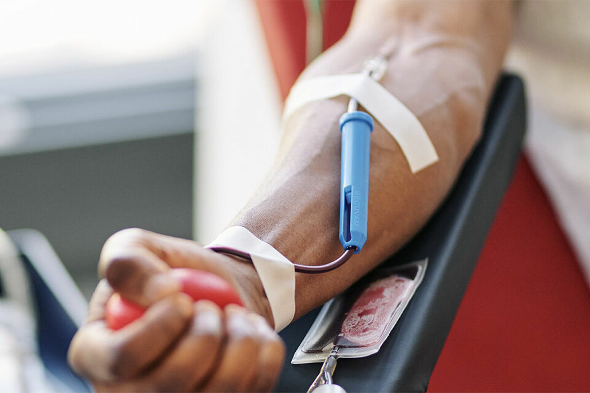 Ein Spender liegt bei einer Blutspende, der Arm ist mit einer Kanüle verbunden und er drückt einen Ball zur Unterstützung des Blutflusses.