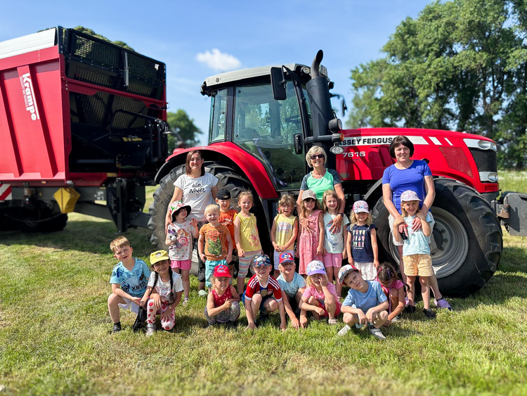 Gruppenfoto von Kindern und Erzieherinnen der DRK-Kita „Rasselbande“ vor einem roten Traktor auf dem Bauernhof in Königsrode.
