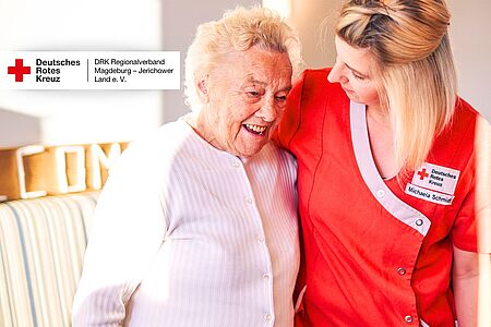 Titelbild zur Stellenausschreibung: Zwei Frauen, eine als DRK-Pflegekraft und eine Seniorin, lachen und gehen Arm in Arm im Seniorenzentrum Möckern.