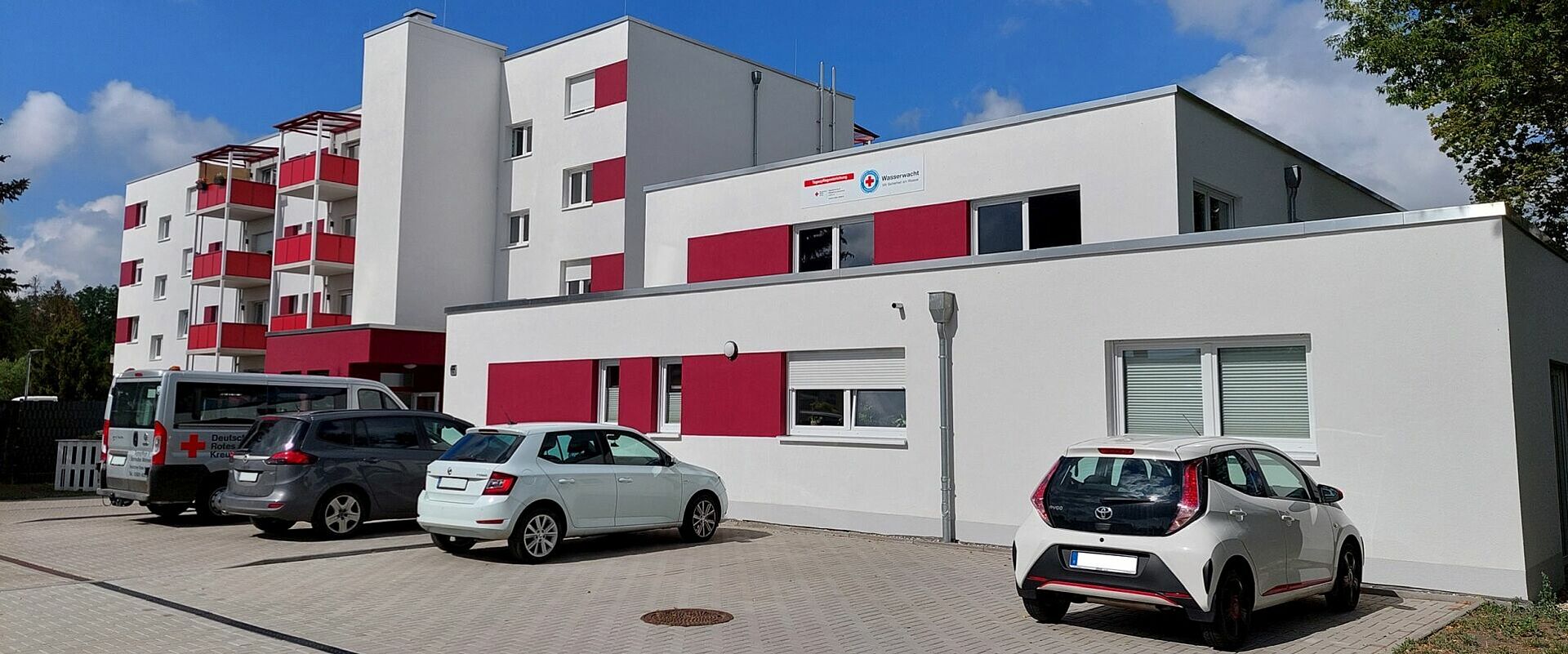Gebäudeansicht der DRK-Tagespflege „Niegripper Chaussee“ (Siedlung) mit Betreutem Wohnen, Parkplatz im Vordergrund.