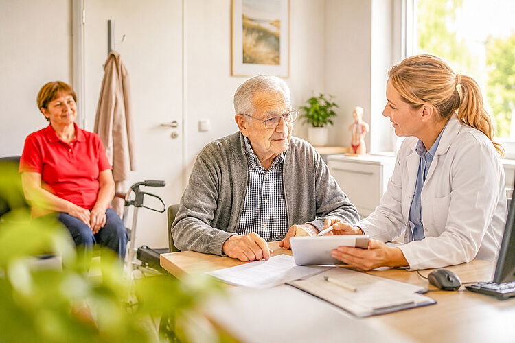 KI-generierte Beispieldarstellung eines Arzttermins mit einem Senior, einer Ärztin und einer dezent wartenden Begleitperson.