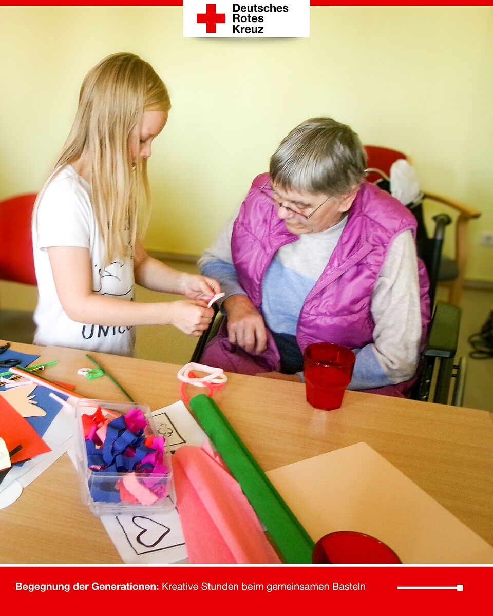 Ein Mädchen reicht einer Seniorin Bastelmaterial, beide lachen dabei.