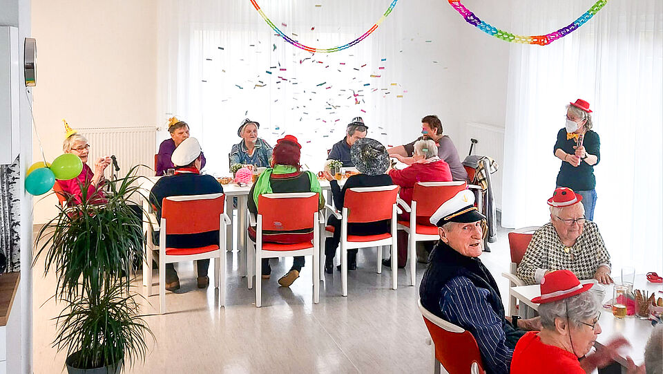 Seniorinnen und Senioren feiern Karneval in der DRK-Tagespflege „Niegripper Chaussee“ (Siedlung), mit Partyhüten, Konfetti und bunter Dekoration.