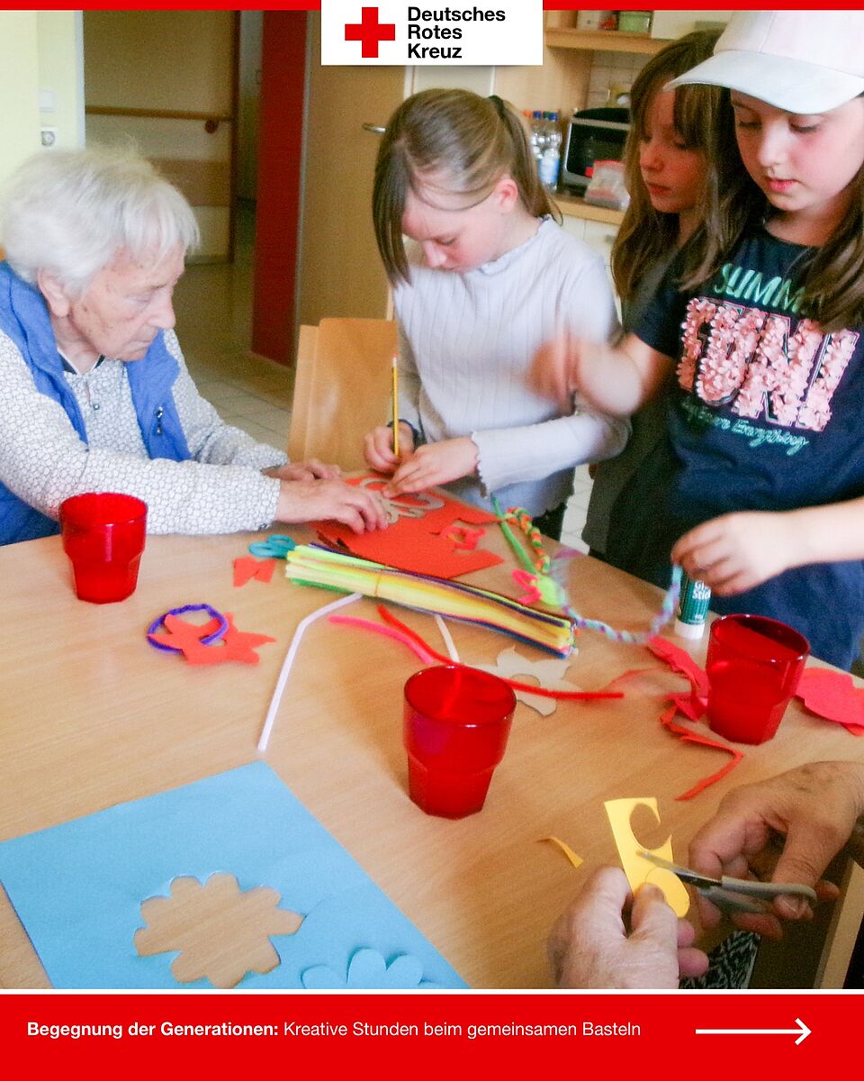 Kinder sitzen mit Seniorinnen am Tisch und schneiden bunte Papierformen aus.